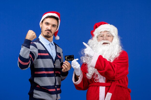 Vista frontal do Papai Noel com jovem segurando o cartão do banco na parede azul