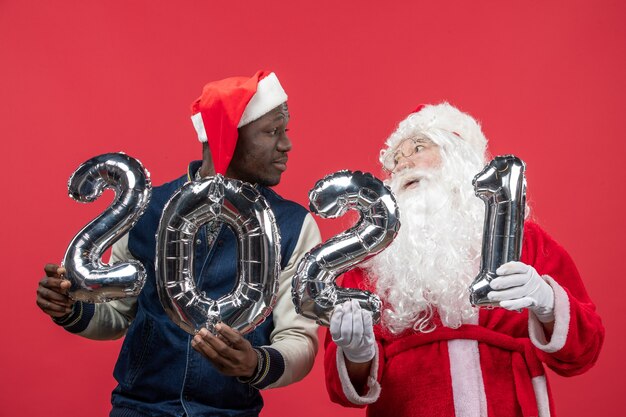 Vista frontal do Papai Noel com jovem segurando uma escrita na parede vermelha