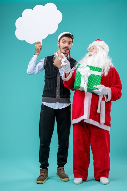 Foto grátis vista frontal do papai noel com jovens homens segurando um cartaz de nuvem branca sobre o fundo azul