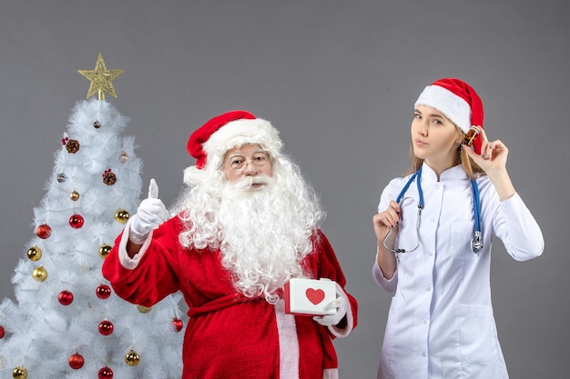 Vista frontal do Papai Noel com médica segurando o frasco com comprimidos na parede cinza