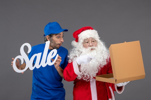 Vista frontal do papai noel com mensageiro masculino segurando banner de venda e caixas de comida na parede cinza