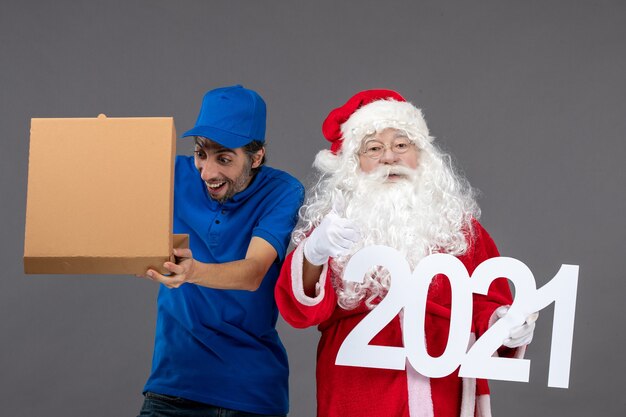 Vista frontal do Papai Noel com mensageiro segurando uma caixa de comida e escrevendo na parede cinza