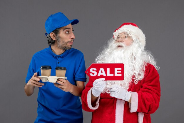 Vista frontal do Papai Noel com o correio masculino segurando a escrita de venda e café na parede cinza