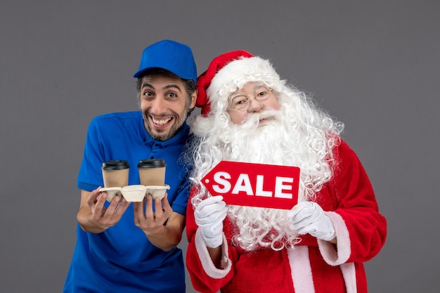 Vista frontal do papai noel com o correio masculino segurando a escrita de venda e café na parede cinza