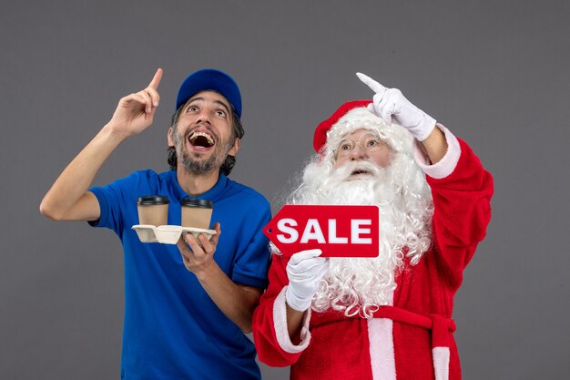 Vista frontal do Papai Noel com o correio masculino segurando a escrita de venda e café na parede cinza