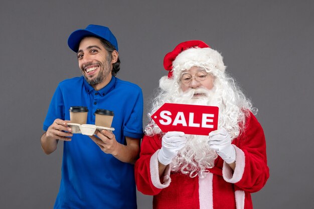 Vista frontal do papai noel com o correio masculino segurando a escrita de venda e café na parede cinza