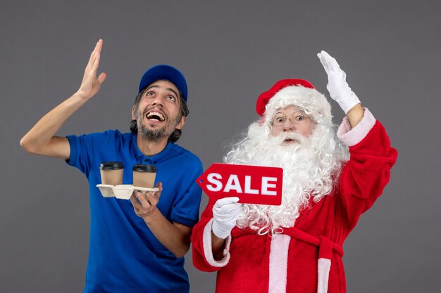 Vista frontal do Papai Noel com o correio masculino segurando a escrita de venda e café na parede cinza