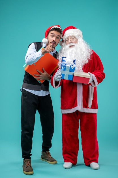 Vista frontal do papai noel com o jovem e presentes na parede azul