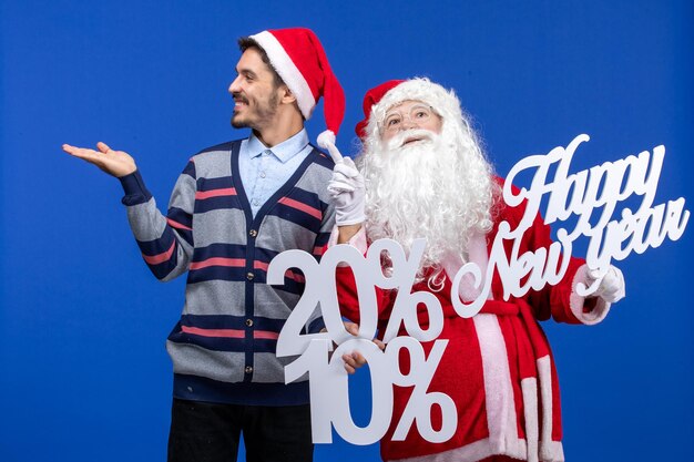 Vista frontal do Papai Noel com o jovem segurando os escritos de feliz ano novo e porcentagem na parede azul