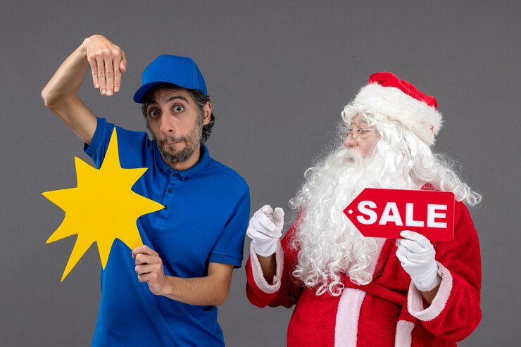 Foto grátis vista frontal do papai noel com o mensageiro masculino segurando a faixa de venda e uma placa amarela na parede cinza