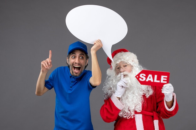 Foto grátis vista frontal do papai noel com o mensageiro segurando uma placa branca e uma faixa de venda na parede cinza