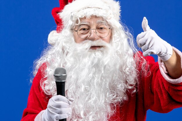 Vista frontal do papai noel com terno vermelho e barba branca segurando o microfone na cor azul feriado de natal ano novo