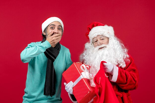 Vista frontal do papai noel com um homem tirando um presente da bolsa em um feriado vermelho natal emoção cor