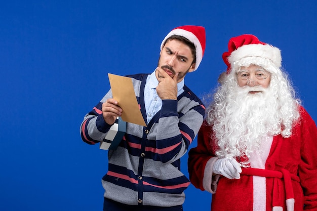 Vista frontal do papai noel com um jovem que está lendo uma carta na parede azul