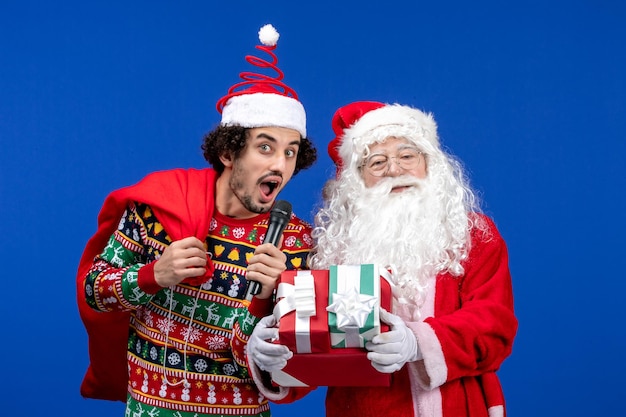 Vista frontal do Papai Noel com um jovem que está usando o microfone na parede azul