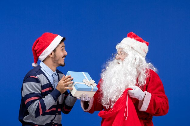 Vista frontal do Papai Noel com um jovem segurando uma sacola de presentes na parede azul