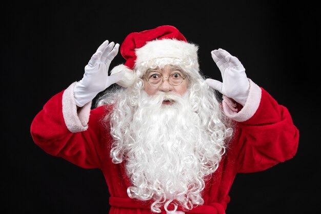 Vista frontal do Papai Noel em um terno vermelho clássico com barba branca na parede preta