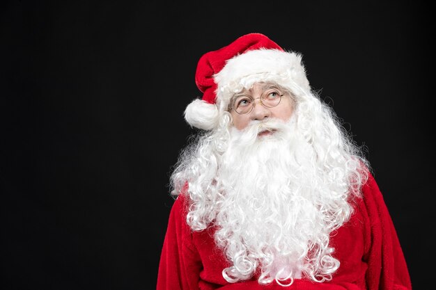 Vista frontal do Papai Noel em um terno vermelho clássico com barba branca na parede preta