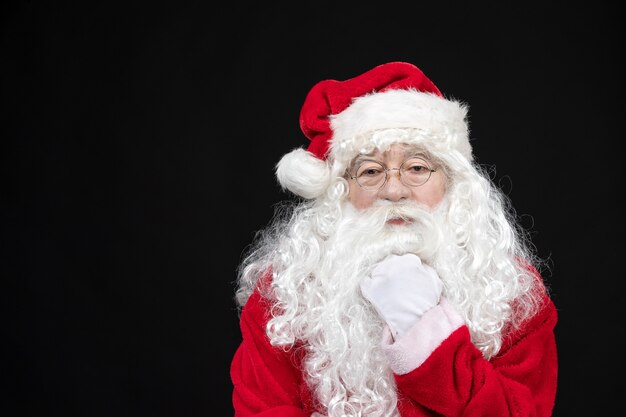Vista frontal do Papai Noel em um terno vermelho clássico com barba branca na parede preta
