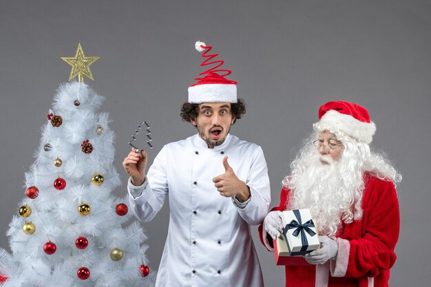 Vista frontal do papai noel em volta da árvore do feriado com cozinheiro