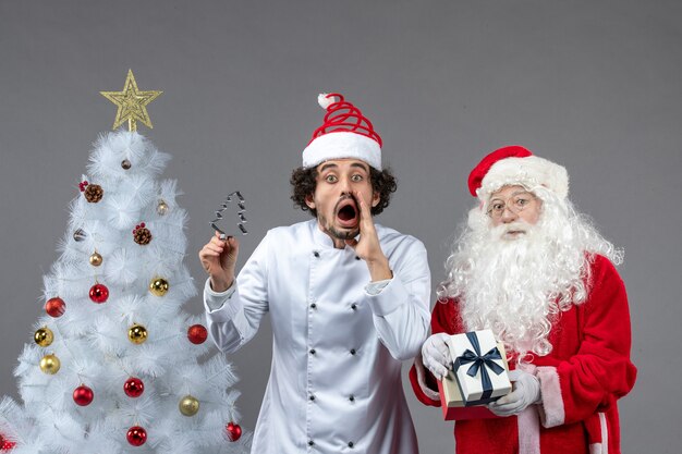 Foto grátis vista frontal do papai noel em volta da árvore do feriado com cozinheiro