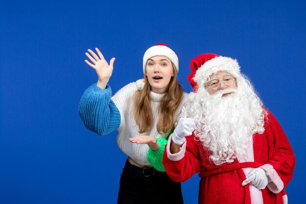 Vista frontal do papai noel junto com a jovem fêmea em pé na cor azul do feriado de ano novo e emoções de natal