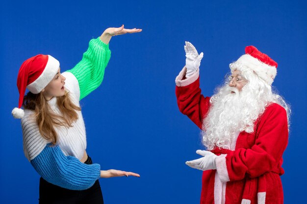 Vista frontal do Papai Noel junto com uma jovem fêmea parada na parede azul