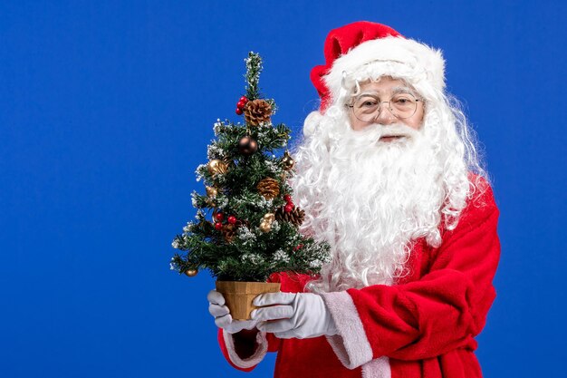 Vista frontal do papai noel segurando a pequena árvore de ano novo no azul de Natal ano novo