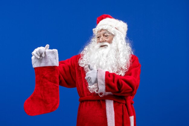 Vista frontal do papai noel segurando uma grande meia de natal na neve de cor azul