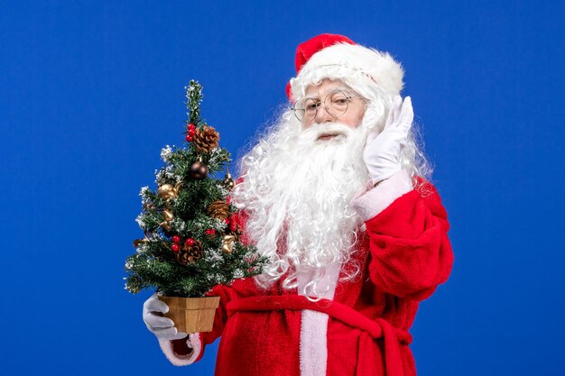 Vista frontal do papai noel segurando uma pequena árvore de ano novo em uma neve azul Natal ano novo
