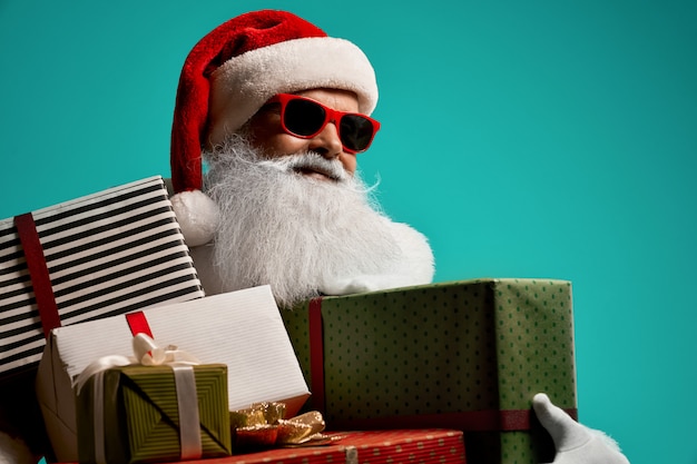 Vista frontal do Papai Noel sorridente com barba branca, aparecendo o polegar. Retrato isolado do homem sênior bonito em traje de Natal e óculos posando conceito de férias.