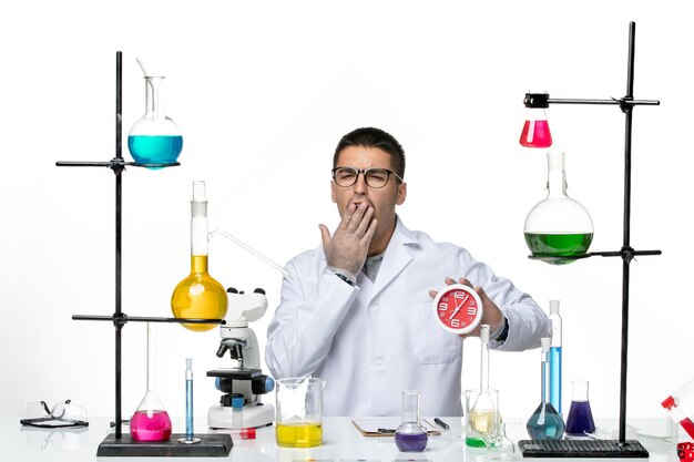 Vista frontal do químico masculino em terno médico branco segurando relógios vermelhos no fundo branco vírus doença ciência laboratório covid