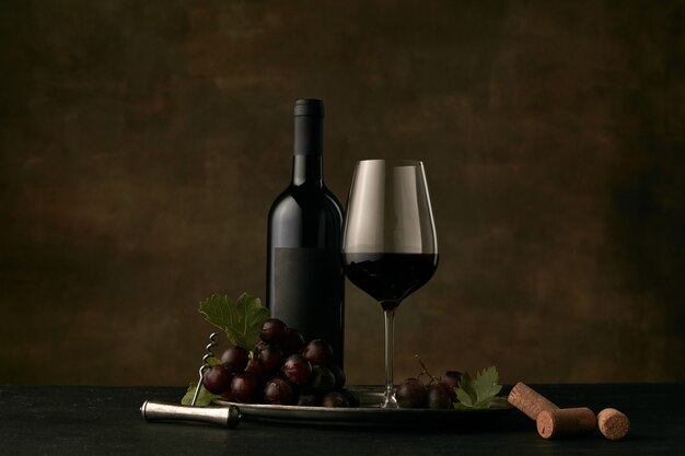 Vista frontal do saboroso prato de frutas de uvas com a garrafa de vinho, queijo, frutas e vidro em fundo escuro