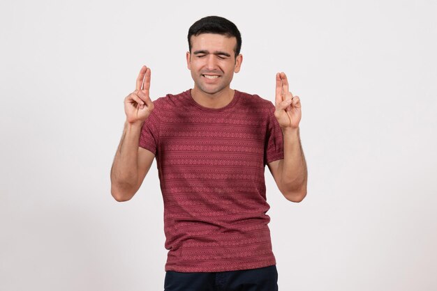 Vista frontal do sexo masculino jovem com camiseta em pé e posando em fundo branco