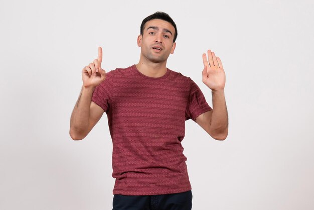 Vista frontal do sexo masculino jovem com camiseta em pé e posando em fundo branco