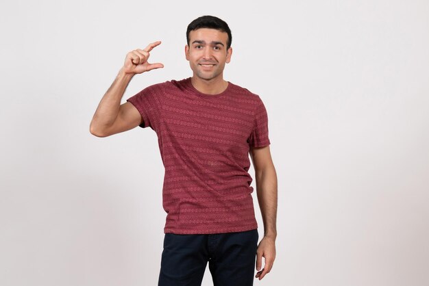 Vista frontal do sexo masculino jovem com camiseta em pé e posando em fundo branco