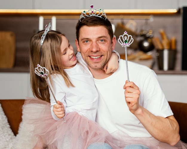 Vista frontal do sorridente pai e filha brincando com a tiara e a varinha