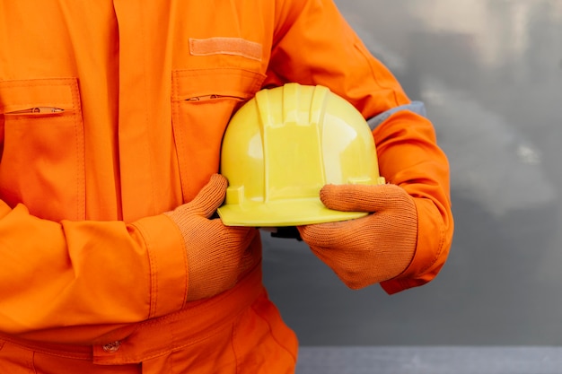 Vista frontal do trabalhador de uniforme segurando capacete