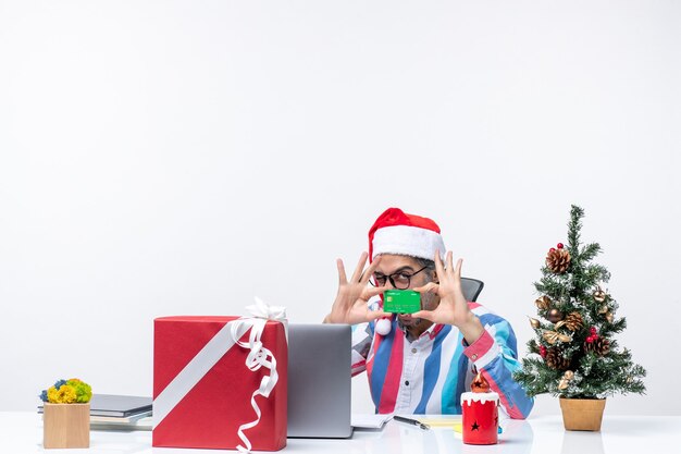 Vista frontal do trabalhador do sexo masculino sentado em seu local de trabalho, segurando o cartão do banco verde dinheiro escritório emoção de Natal