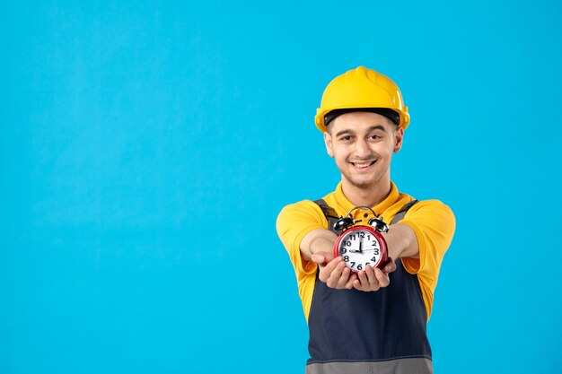 Vista frontal do trabalhador masculino feliz em uniforme amarelo com relógios na parede azul