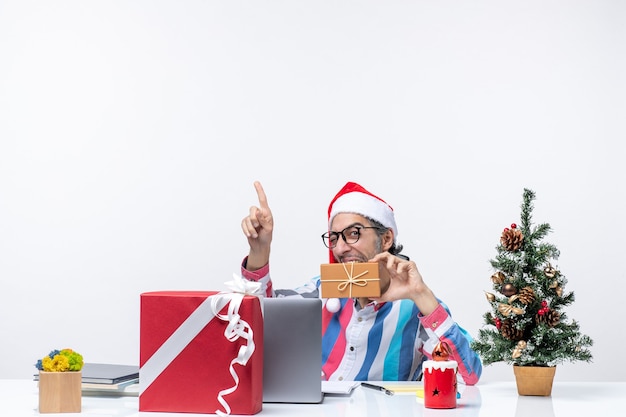 Foto grátis vista frontal do trabalhador masculino sentado em seu local de trabalho segurando pacote emoções natal trabalho feriado escritório