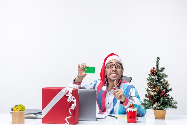 Vista frontal do trabalhador masculino sentado em seu local de trabalho, segurando um emprego de cartão de banco verde Natal dinheiro emoção