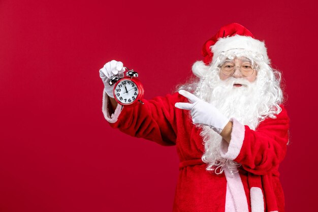 Vista frontal do velho papai noel em terno vermelho segurando o relógio na parede vermelha