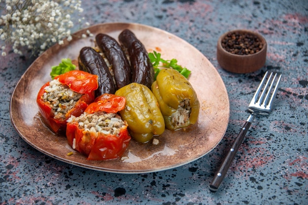 vista frontal dolma de berinjela com tomates cozidos e pimentões recheados com carne moída dentro do prato sobre fundo azul alimento prato cor jantar refeição