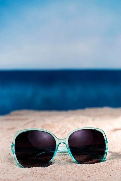 Vista frontal dos óculos de sol na areia da praia, com espaço de cópia