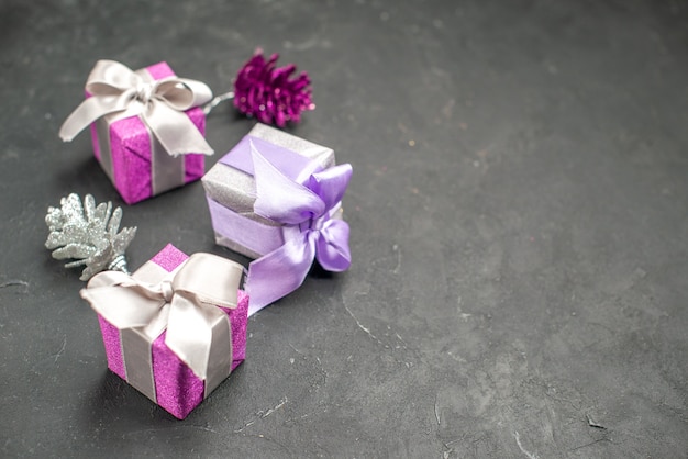 Vista frontal dos presentes de Natal rosa e roxo com fitas brinquedos da árvore de Natal no espaço livre de fundo escuro isolado