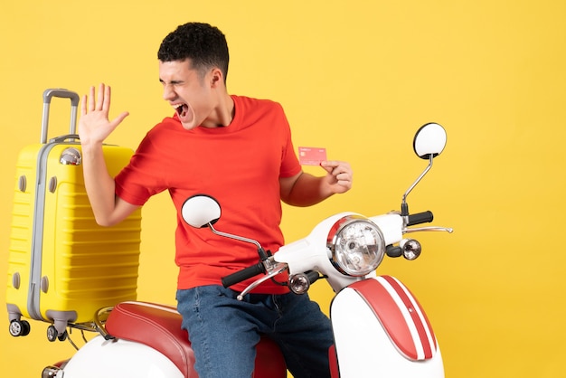 Vista frontal espantado jovem numa motocicleta segurando cartão de crédito