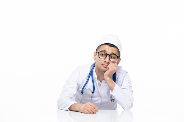 Vista frontal estressado médico masculino em terno médico sentado atrás de uma mesa