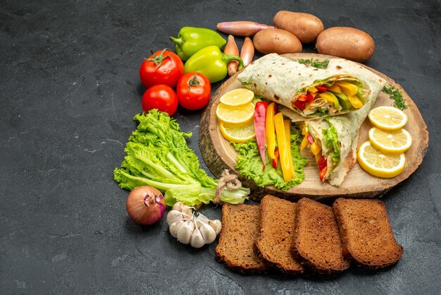 Vista frontal fatiado delicioso sanduíche de carne shaurma com pão e vegetais no espaço escuro