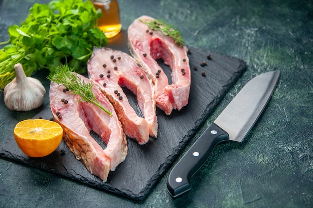 Vista frontal fatias de peixe fresco com verdes na superfície azul-escuro refeição carne do oceano cor crua jantar água frutos do mar foto